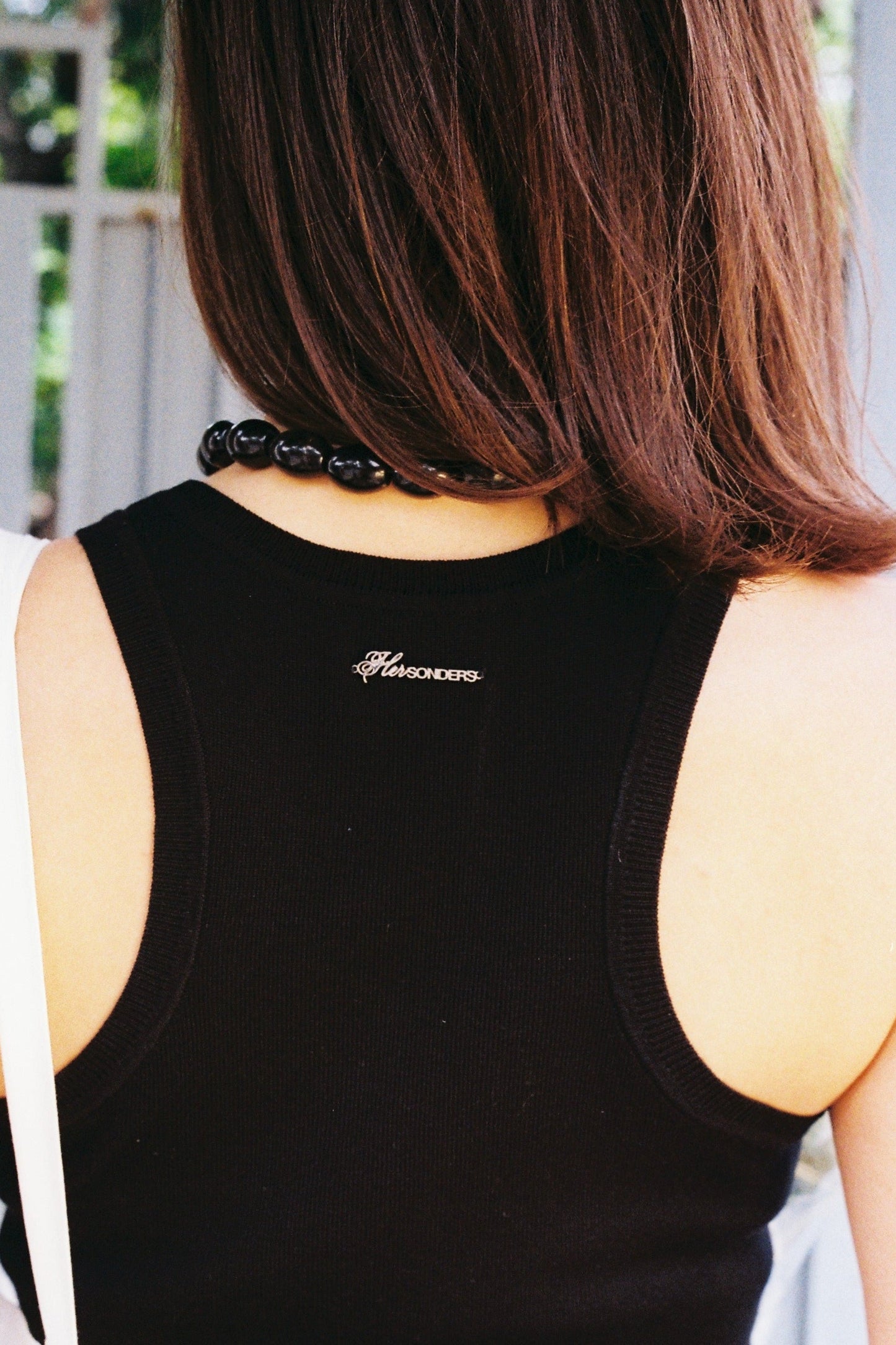 Person wearing a black tank top with a brand logo, standing outdoors.